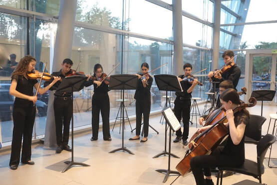 Young musicians playing their string instruments in the Music Center glass-encased lobby